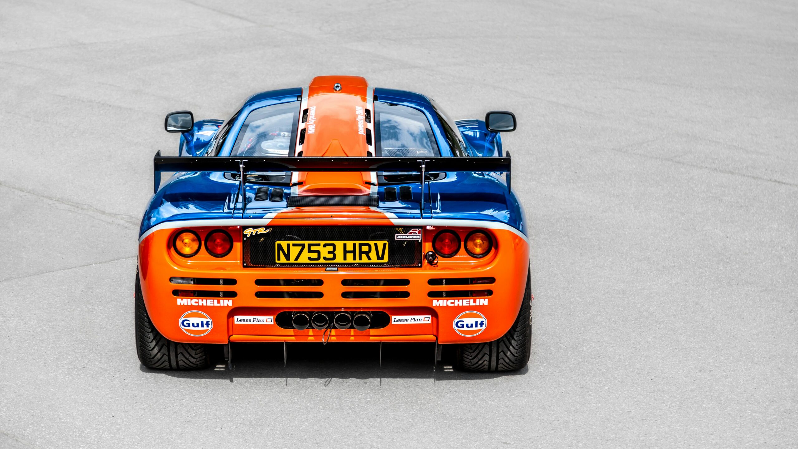 A striking rear view of a classic blue and orange McLaren sports car on display.